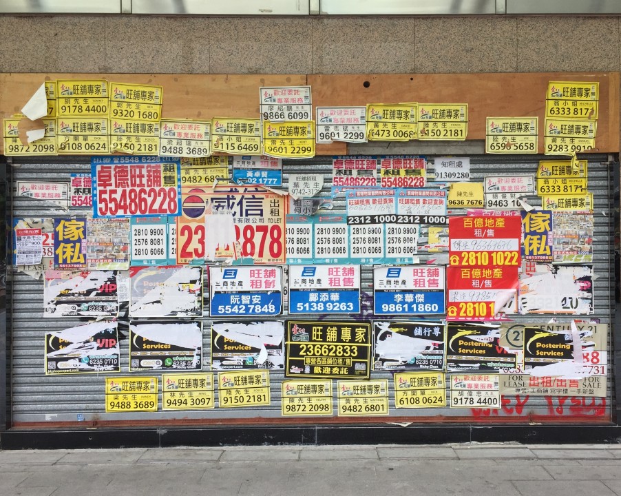 A Hong Kong shopfront shutter covered in property agent advertisement flyers.